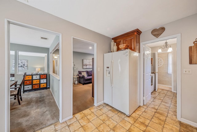 kitchen featuring brown cabinets, stone finish floor, white fridge with ice dispenser, and baseboards