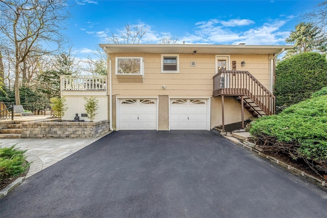 back of house with an attached garage, driveway, and stairs