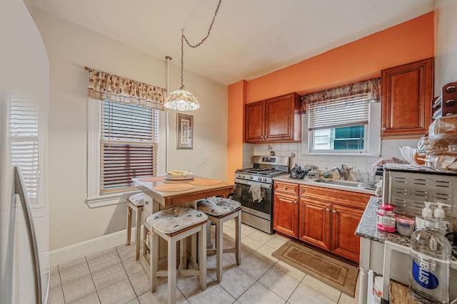 kitchen featuring a sink, decorative backsplash, light tile patterned floors, stainless steel gas stove, and baseboards