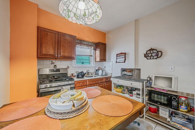 kitchen featuring tasteful backsplash, a sink, brown cabinetry, black microwave, and stainless steel gas range oven