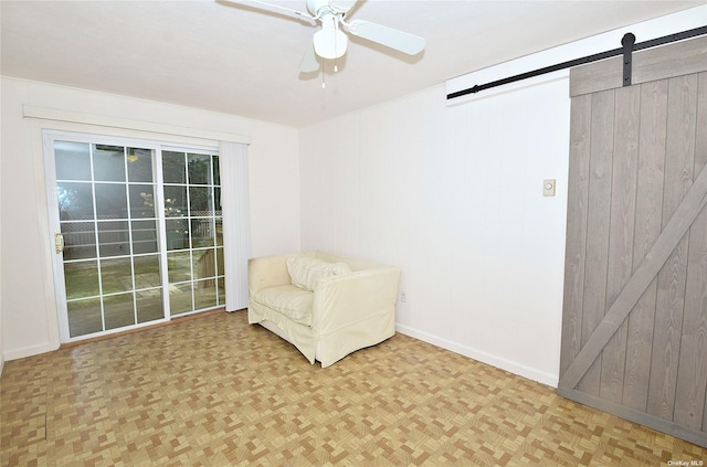unfurnished room featuring wooden walls, baseboards, a ceiling fan, and a barn door