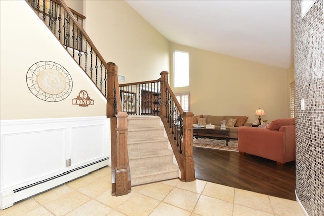 staircase with baseboard heating, high vaulted ceiling, and a wainscoted wall