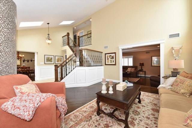living area with stairway, visible vents, a skylight, high vaulted ceiling, and wood finished floors