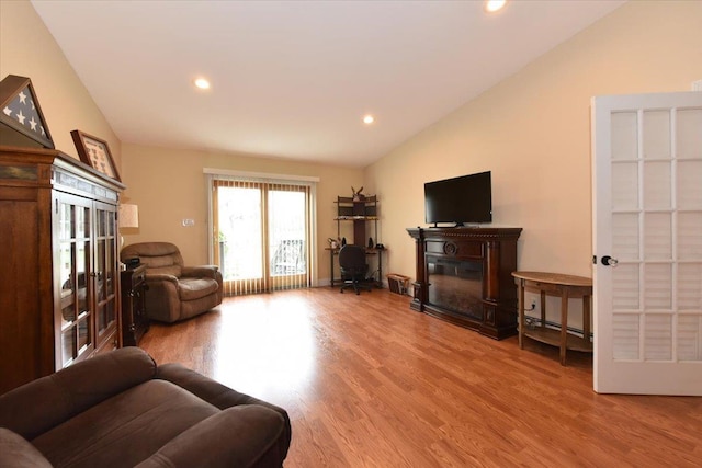 living area featuring light wood finished floors, a glass covered fireplace, recessed lighting, and lofted ceiling