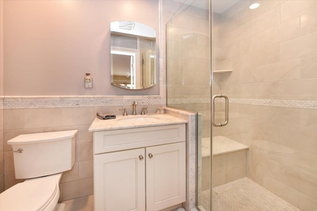 bathroom featuring toilet, tile walls, wainscoting, vanity, and a stall shower