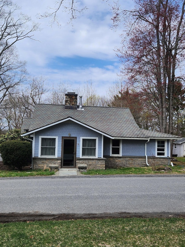 view of front of home featuring roof with shingles, stone siding, and a chimney