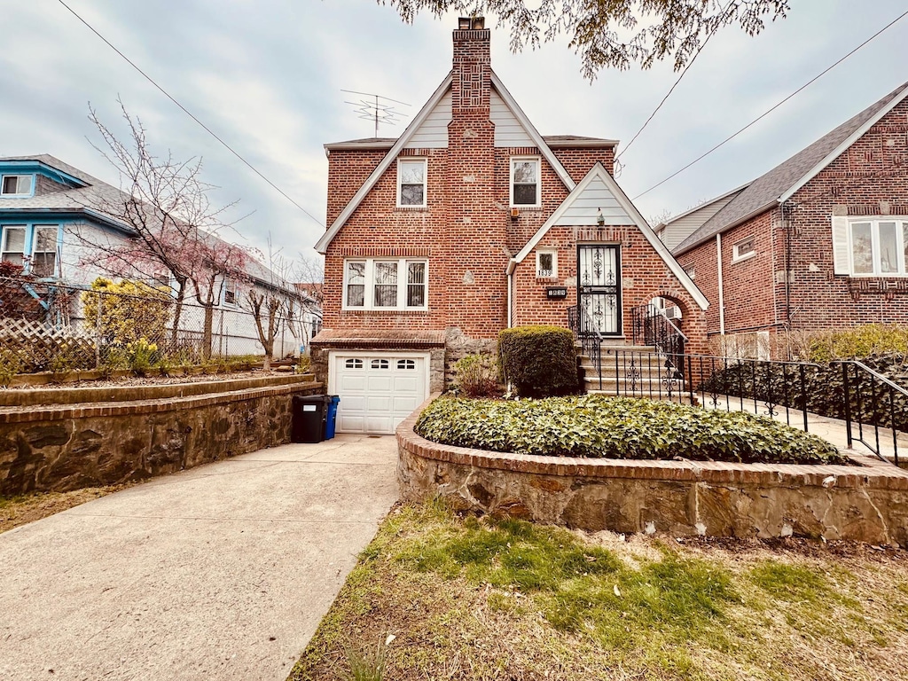 tudor house featuring fence, brick siding, an attached garage, a chimney, and driveway