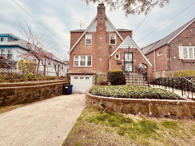 tudor house featuring fence, brick siding, an attached garage, a chimney, and driveway