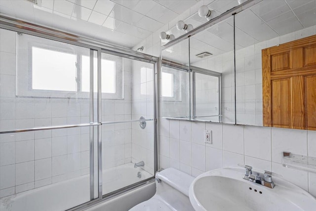 bathroom with a sink, toilet, tile walls, combined bath / shower with glass door, and tasteful backsplash