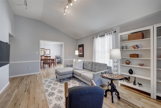 living area with track lighting, light wood-type flooring, baseboards, and vaulted ceiling