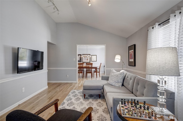 living room featuring lofted ceiling, baseboards, track lighting, and wood finished floors