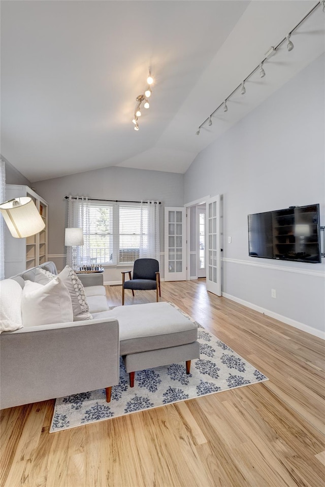 living area with french doors, vaulted ceiling, baseboards, wood finished floors, and rail lighting