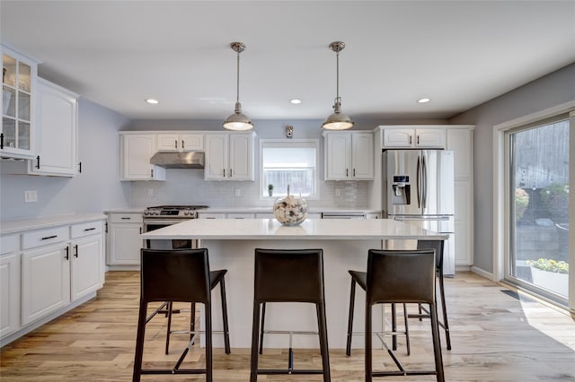 kitchen featuring tasteful backsplash, glass insert cabinets, stainless steel appliances, a kitchen bar, and under cabinet range hood