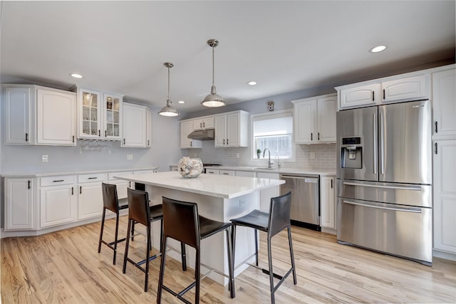 kitchen with light wood finished floors, stainless steel appliances, a kitchen breakfast bar, and under cabinet range hood