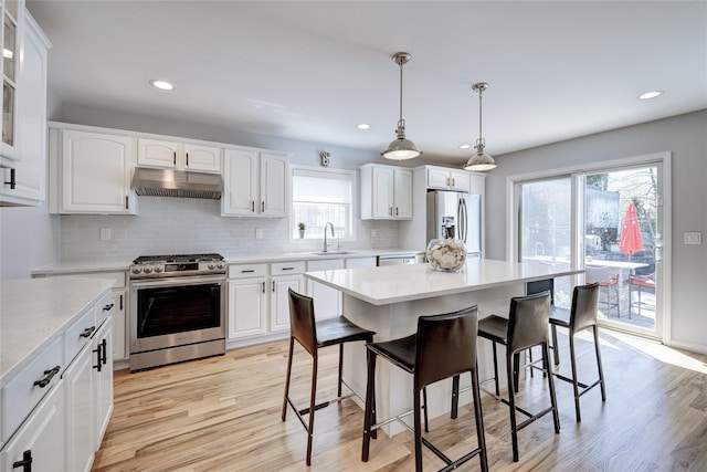 kitchen featuring stainless steel appliances, a sink, decorative backsplash, a breakfast bar, and under cabinet range hood