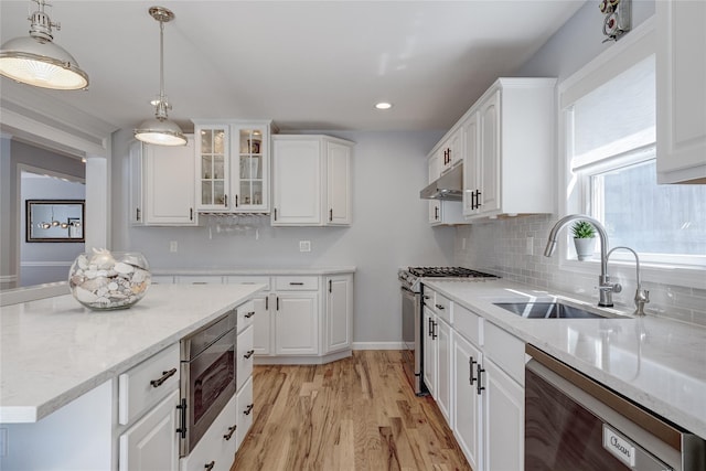 kitchen featuring white cabinets, a sink, light wood-style floors, under cabinet range hood, and appliances with stainless steel finishes