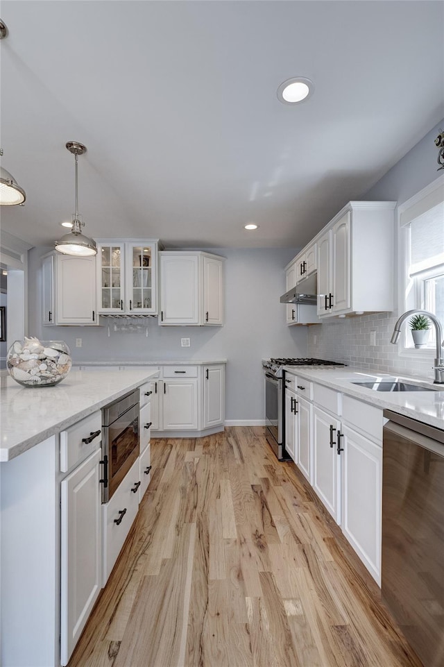 kitchen featuring under cabinet range hood, stainless steel appliances, a sink, light wood-style floors, and white cabinetry