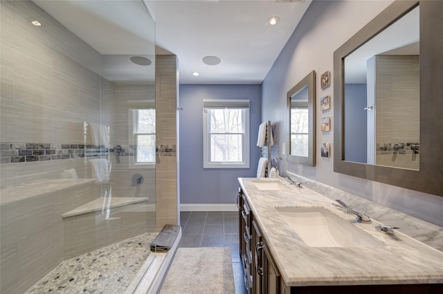bathroom with baseboards, a sink, double vanity, and tiled shower