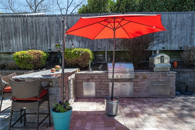 view of patio / terrace with an outdoor kitchen, grilling area, fence, and outdoor wet bar