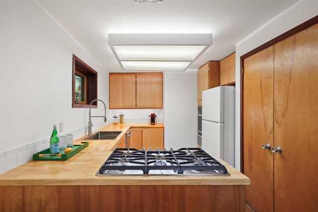 kitchen featuring gas stovetop, a sink, freestanding refrigerator, a peninsula, and wood counters