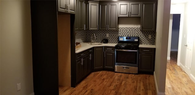 kitchen featuring a sink, light countertops, wood finished floors, stainless steel gas range oven, and decorative backsplash