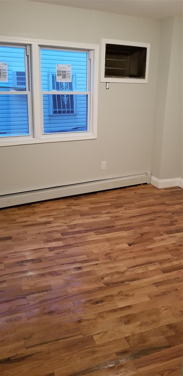 spare room featuring a baseboard radiator, a wall mounted air conditioner, wood finished floors, and baseboards