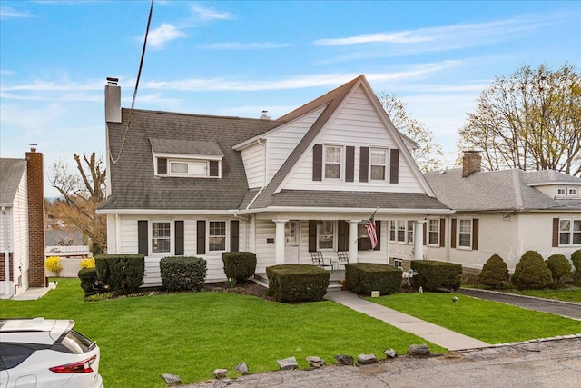 shingle-style home featuring a front yard, a porch, a chimney, and a shingled roof