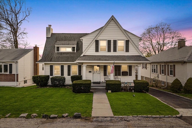 view of front of property featuring driveway, covered porch, a lawn, and roof with shingles