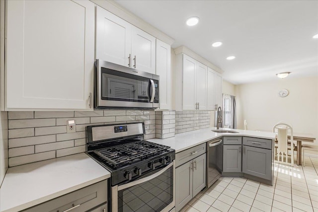kitchen featuring a sink, appliances with stainless steel finishes, gray cabinetry, and a peninsula