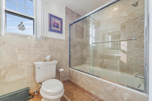 bathroom with tile walls, toilet, tiled shower / bath, and a healthy amount of sunlight