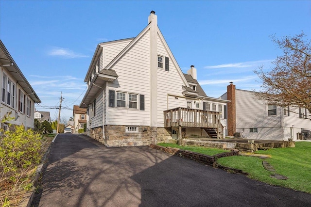 rear view of house with aphalt driveway, a deck, a chimney, and stairs