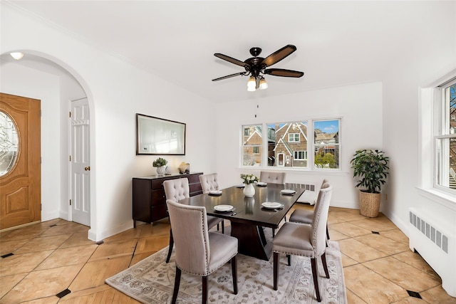 dining room featuring light tile patterned floors, baseboards, arched walkways, a ceiling fan, and radiator