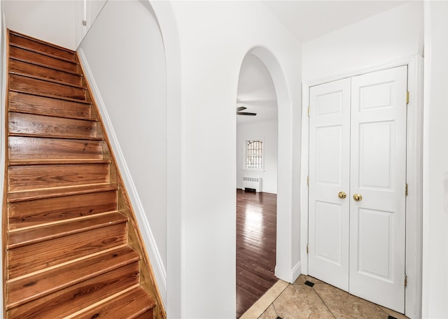 staircase with arched walkways, radiator, wood finished floors, and baseboards
