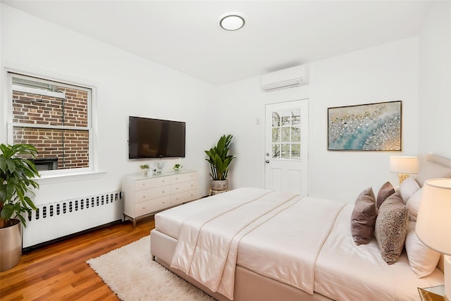 bedroom with radiator heating unit, a wall mounted AC, and wood finished floors