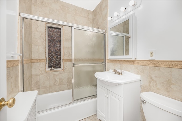 bathroom featuring toilet, vanity, combined bath / shower with glass door, and tile walls