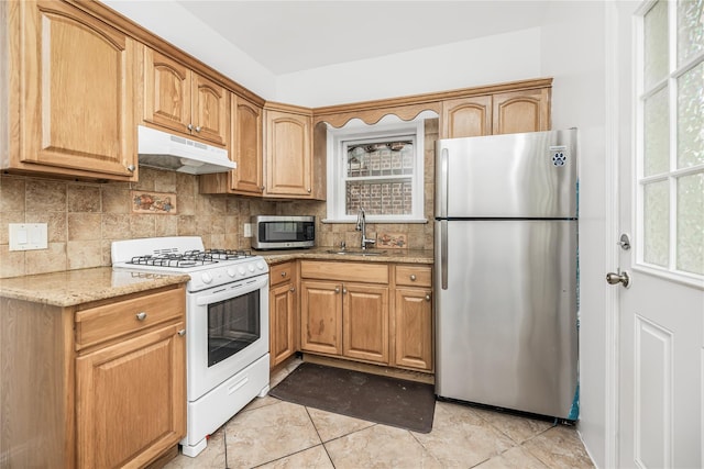 kitchen with a sink, appliances with stainless steel finishes, under cabinet range hood, light stone countertops, and decorative backsplash