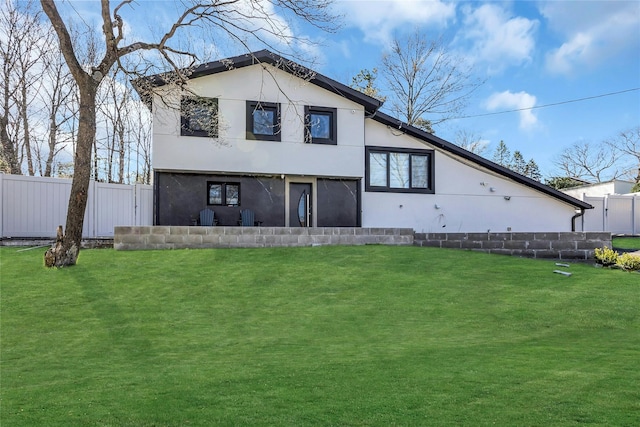 rear view of house with stucco siding, a lawn, and fence