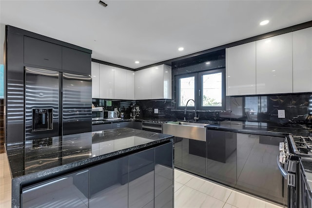 kitchen featuring stainless steel appliances, a sink, modern cabinets, tasteful backsplash, and white cabinetry