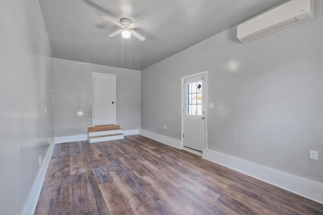 spare room featuring a wall mounted air conditioner, ceiling fan, baseboards, and wood finished floors
