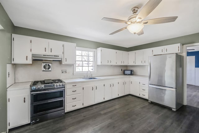 kitchen with a sink, dark wood-style flooring, a ceiling fan, under cabinet range hood, and appliances with stainless steel finishes