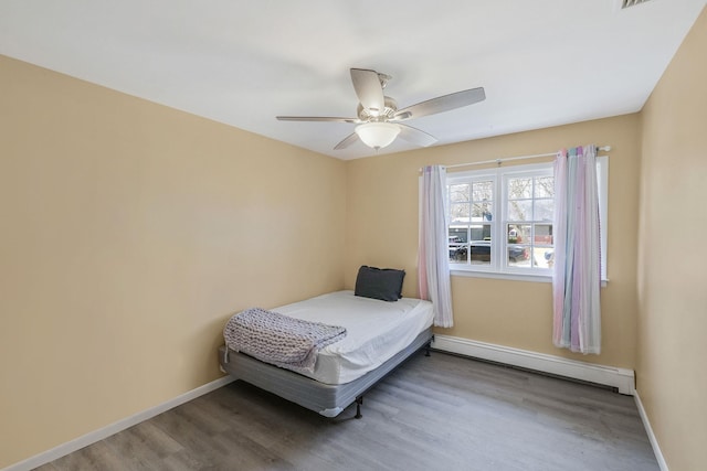 bedroom featuring a baseboard heating unit, wood finished floors, baseboards, and ceiling fan