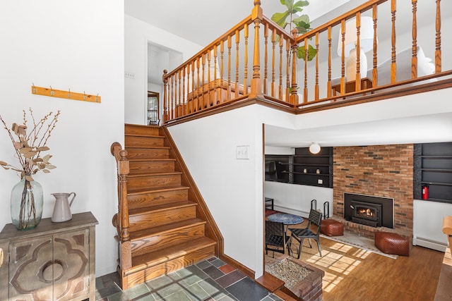 stairs featuring a baseboard radiator, baseboards, a brick fireplace, and a towering ceiling