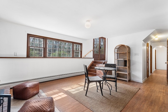 dining room with a baseboard heating unit, wood finished floors, baseboards, and stairway
