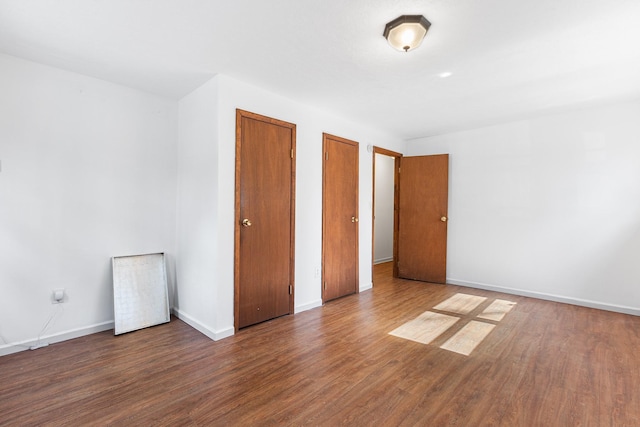 unfurnished bedroom with multiple closets, baseboards, and wood finished floors