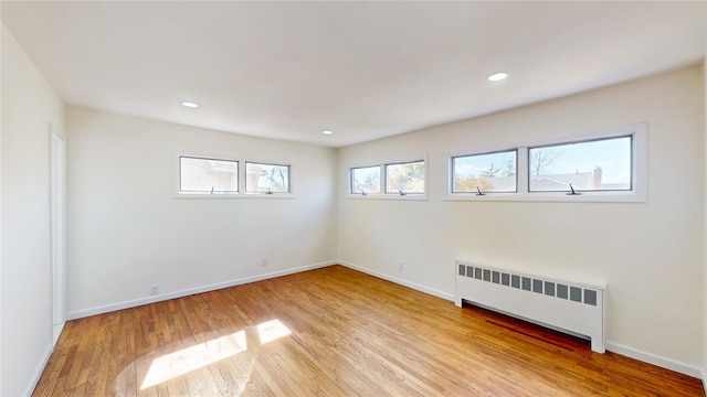 spare room featuring recessed lighting, baseboards, radiator heating unit, and light wood-style floors