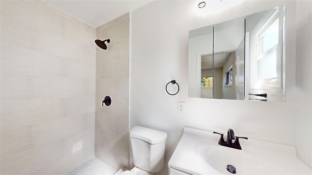 full bathroom with toilet, tiled shower, and vanity