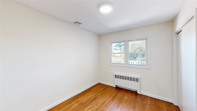 unfurnished room featuring baseboards, radiator, light wood-style floors, and visible vents