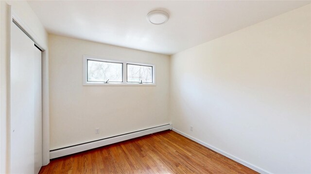 unfurnished bedroom with baseboards, a baseboard radiator, a closet, and wood finished floors
