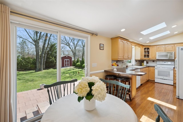 dining space with recessed lighting, lofted ceiling with skylight, a healthy amount of sunlight, and light wood finished floors