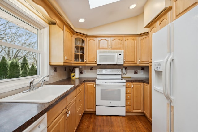 kitchen featuring a sink, vaulted ceiling with skylight, white appliances, and tasteful backsplash
